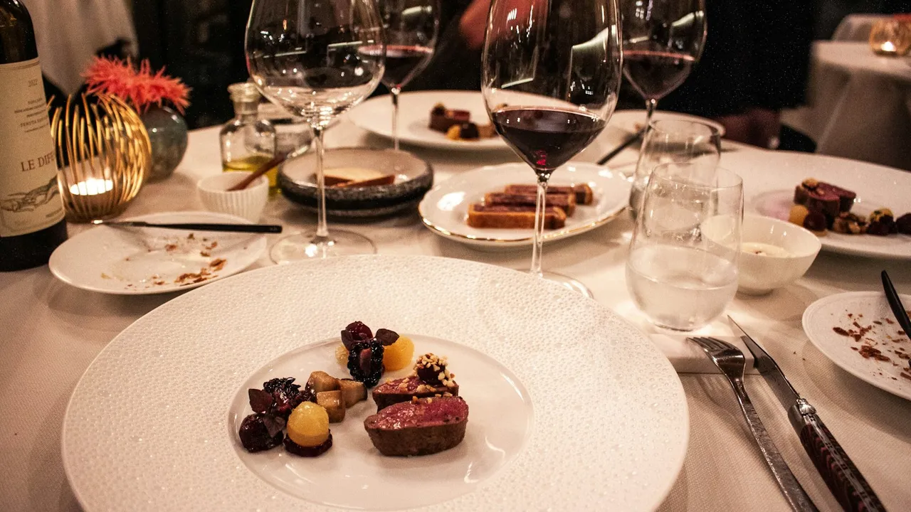 Mesa de restaurante com prato de carne, taças de vinho tinto e louça branca
